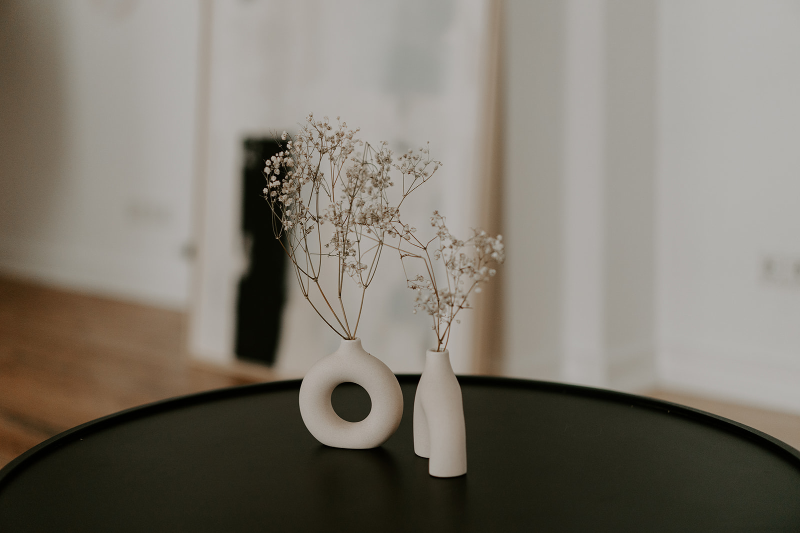 Auf einem schwarzen Tisch stehen weiße Vasen mit Trockenblumen