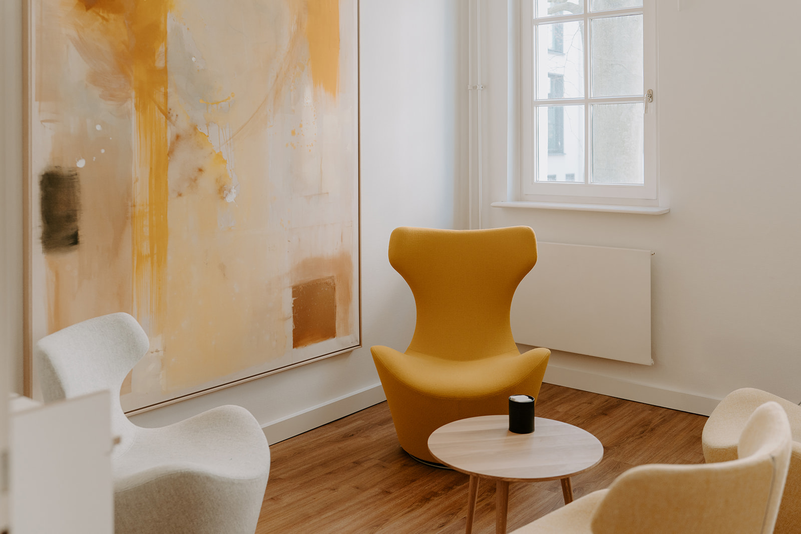 Eine Sitzgruppe aus drei Designer-Sesseln in gelb und beige mit einem schönen abstrakten Gemälde in passenden Tönen an der Wand